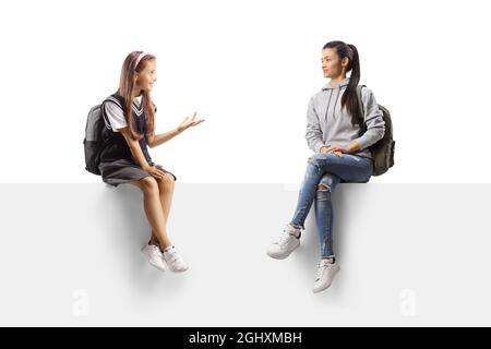 Little schoolgirl talking to a young female student and sitting on a blank panel isolated on white background Stock Photo