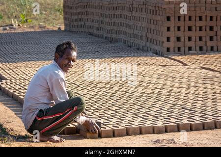 TIKAMGARH, MADHYA PRADESH, INDIA - AUGUST 11, 2021: Indian man making house bricks by hand using a mold and wet clay. Stock Photo