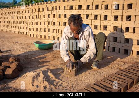 TIKAMGARH, MADHYA PRADESH, INDIA - AUGUST 11, 2021: Indian man making house bricks by hand using a mold and wet clay. Stock Photo