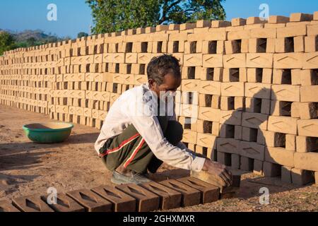 TIKAMGARH, MADHYA PRADESH, INDIA - AUGUST 11, 2021: Indian man making house bricks by hand using a mold and wet clay. Stock Photo