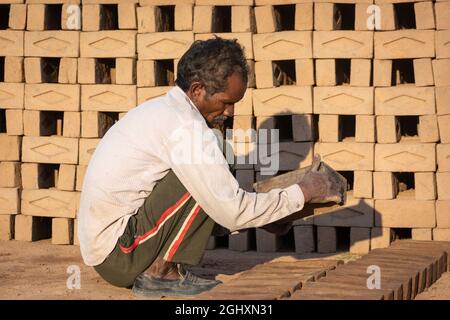 TIKAMGARH, MADHYA PRADESH, INDIA - AUGUST 11, 2021: Indian man making house bricks by hand using a mold and wet clay. Stock Photo