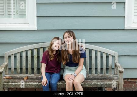 Two sisters embracing and hugging on a bench outside Stock Photo