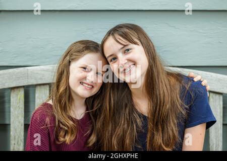 Two sisters embracing and hugging on a bench outside Stock Photo