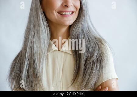 Middle aged woman with long silver hair smiles on light grey background Stock Photo