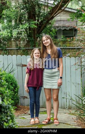 Two sisters embracing and hugging while standing outside in the backyard. Stock Photo