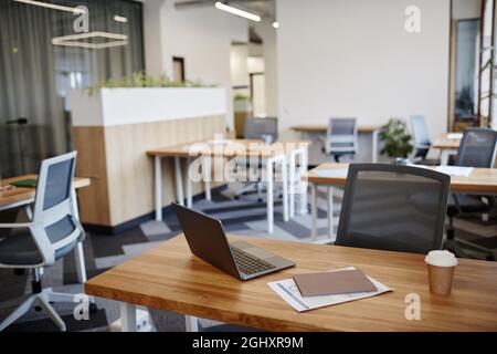 Desk with laptop, cup of coffee and report in empty office in modern building Stock Photo