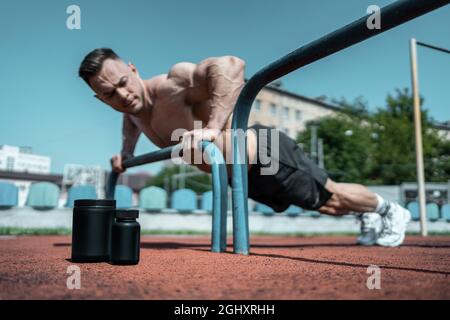 protein whey drink in black container and muscular athlete exercising outdoor Stock Photo