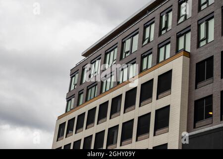 Angled view of a large, window covered apartment building corner against a blue, cloud filled sky Stock Photo