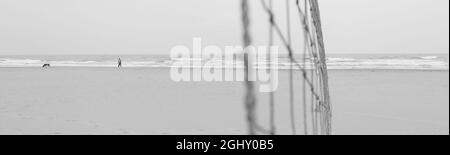 Grayscale shot of a sandy beach and a large volleyball net Stock Photo