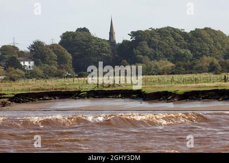 The Solway Bore travelling along the channel of the River Eden with Rockcliffe village in the background Stock Photo