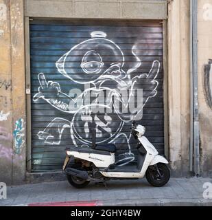 Tel Aviv, Israel - August 17th, 2021:A white motor scooter parked outside a closed shop with a graffiti on a Tel Aviv, Israel, street. Stock Photo
