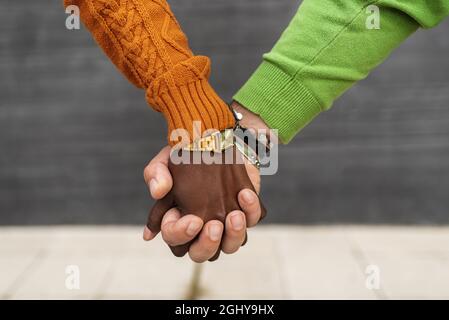 Close up view of an interracial couple holding hands outdoors on the street. Stock Photo