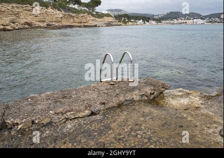 metallic pool ladder on the rocks of the beach on the coast of the town of Moraira, in the province of Alicante, Spain. view Stock Photo