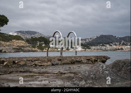 metallic pool ladder on the rocks of the beach on the coast of the town of Moraira, in the province of Alicante, Spain. view Stock Photo