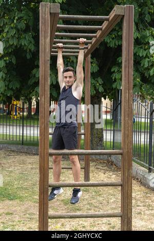 young athlete performing calisthenics exercises with hands through wooden bars placed in the garden Stock Photo