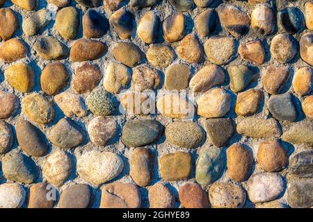 multi-colored and multi-textured pebble stones lie in rows partially pressed into the main covering of a horizontal or vertical surface Stock Photo