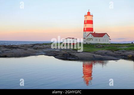 Pointe-des-Monts Lighthouse at sunset with reflections in the sea, Cote-Nord, Quebec Stock Photo