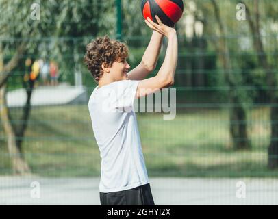 Cute teenager plays basketball at city playground. A boy holds basketball ball in his hands outside. Active life, hobby, sports for children Stock Photo