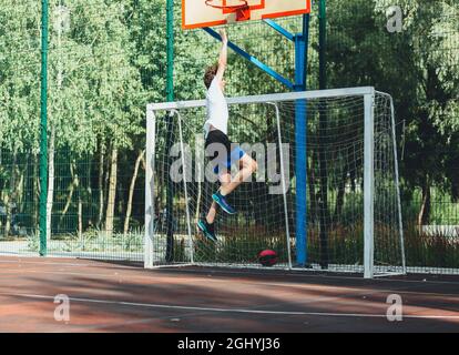 Cute teenager plays basketball at city playground. A boy holds basketball ball in his hands outside. Active life, hobby, sports for children Stock Photo