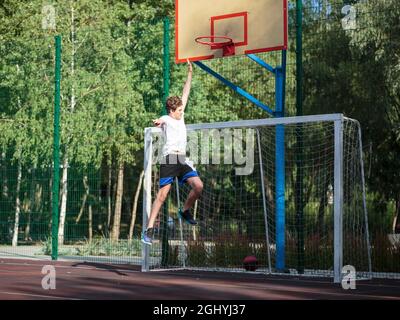 Cute teenager plays basketball at city playground. A boy holds basketball ball in his hands outside. Active life, hobby, sports for children Stock Photo