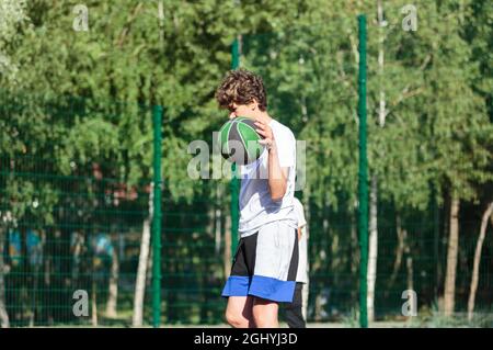 Cute teenager plays basketball at city playground. A boy holds basketball ball in his hands outside. Active life, hobby, sports for children Stock Photo