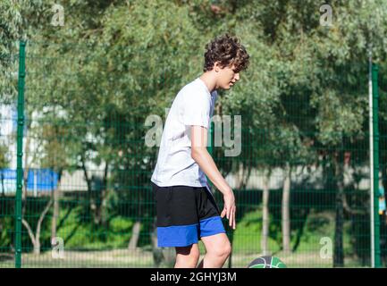 Cute teenager plays basketball at city playground. A boy holds basketball ball in his hands outside. Active life, hobby, sports for children Stock Photo