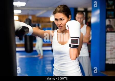 Asian female practicing punches with boxing bag at gym Stock Photo