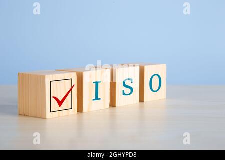 The abbreviation ISO on wooden cubes with check mark on blue background. ISO quality control certification approval concept. Stock Photo