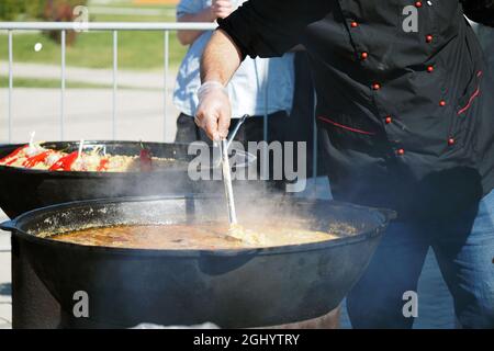 The cook cooks food outside in large vats on coals in the open air Stock Photo