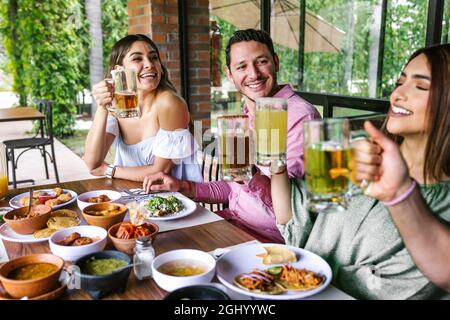 Group of Young latin Friends Meeting For beer, michelada Drinks And mexican Food Making A Toast In Restaurant terrace in Mexico Latin America Stock Photo