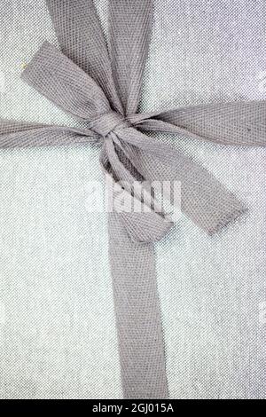 Close up cute grey ribbon bow on a grey linnen package. High quality photo Stock Photo