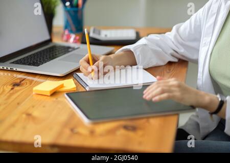 Female architecture taking notes on notepads, looking at tablet screen on table, architects and engineers office workspace, close up Stock Photo