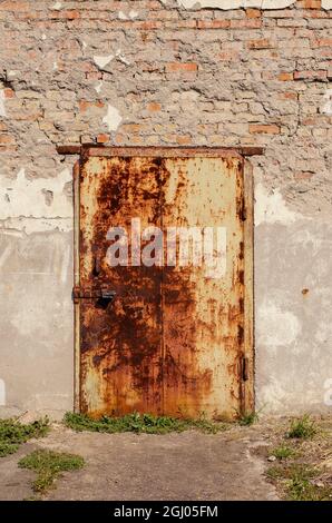 An old rusty metal door in a stone wall. The front door is locke Stock Photo