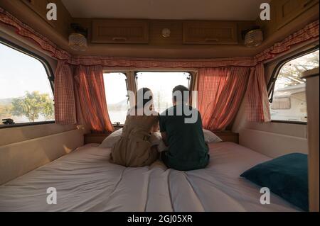 Rear of young couple sitting and taking a view on mattress inside of camper van Stock Photo