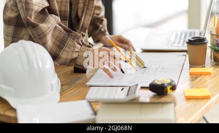 Female architect using divider compass to measuring layout building in engineers office, hardhat, calculator, measurement, architect equipments on wor Stock Photo