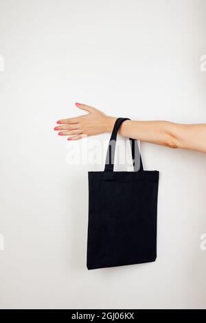 Female hand holding cotton eco-bag. Mockup of small black reusable eco-bag made of recycled materials on white insulated background with space for Stock Photo