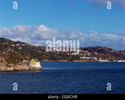 Norwegian Houses on the Fjord sides set amongst trees and rocky outcrops, with a yellow painted wooden House close to the Waters edge. Stock Photo