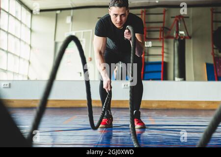 Muscular man in the gym with ropes doing exercises. Crossfit Stock Photo