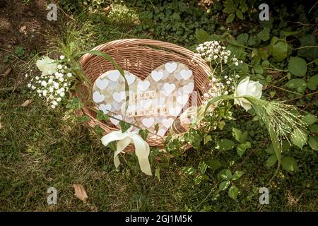 woven basket with white flowers and a heart with the words Just married made of single wooden letters on a green lawn at wedding celebration Stock Photo