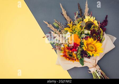Fall bouquet of yellow red orange flowers wrapped in paper and arranged on background. Sunflowers, zinnias and grasses Stock Photo