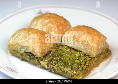 Delicious closeup pistachio baklava on a white dish. One of them has been cut in half to show its pistachios. Stock Photo