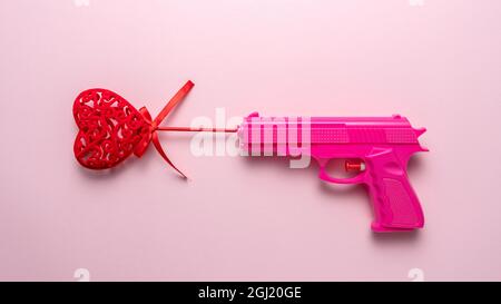 Red heart with Pink gun on pink pastel background. Minimal love concept. Stock Photo