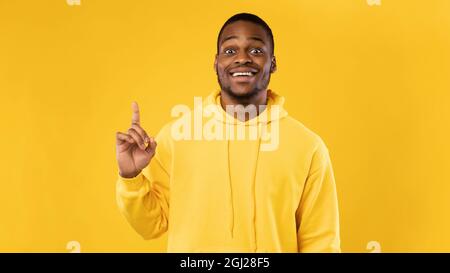 Great Idea. Excited African American Guy Pointing Finger Up Having Thought And Inspiration Posing Standing Over Yellow Studio Background. Eureka Momen Stock Photo