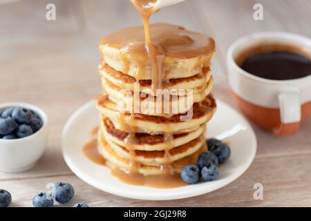 Caramel sauce pouring over pancakes stack, sweet breakfast food Stock Photo