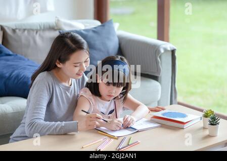 Asian mother teaching her cute kid daughter to studying in living room at home Stock Photo