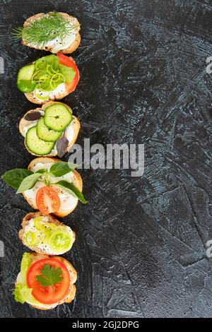 flat lay with vegetable sandwiches with cream cheese, tomatoes, dill, cucumbers, leeks and basil. serving vegetarian sandwiches for appetizers on black background. top view Stock Photo