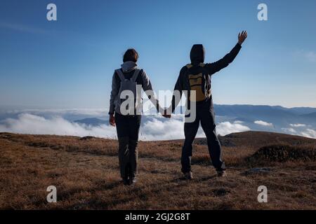 Hiking adventure healthy outdoors people standing talking. Couple enjoying view above clouds on trek. young woman and man in nature wearing hiking bac Stock Photo