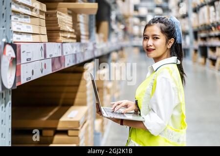 Smiling engineer woman check stock details on tablet for checking boxes with logistics on shelves Stock Photo