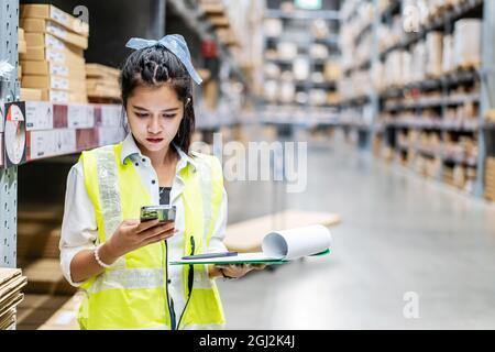 Young woman worker uses the phone for business contacts and holding clipboard to checking inventory Stock Photo
