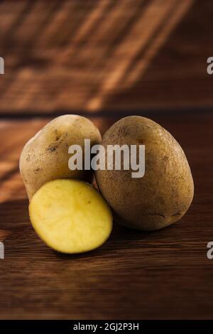 Closeup shot of a sliced potato and whole potatoes on a wooden table Stock Photo
